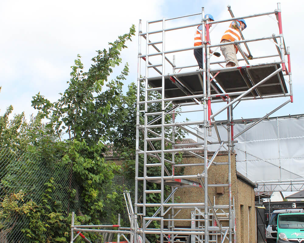 two workman on cantilever access tower outside